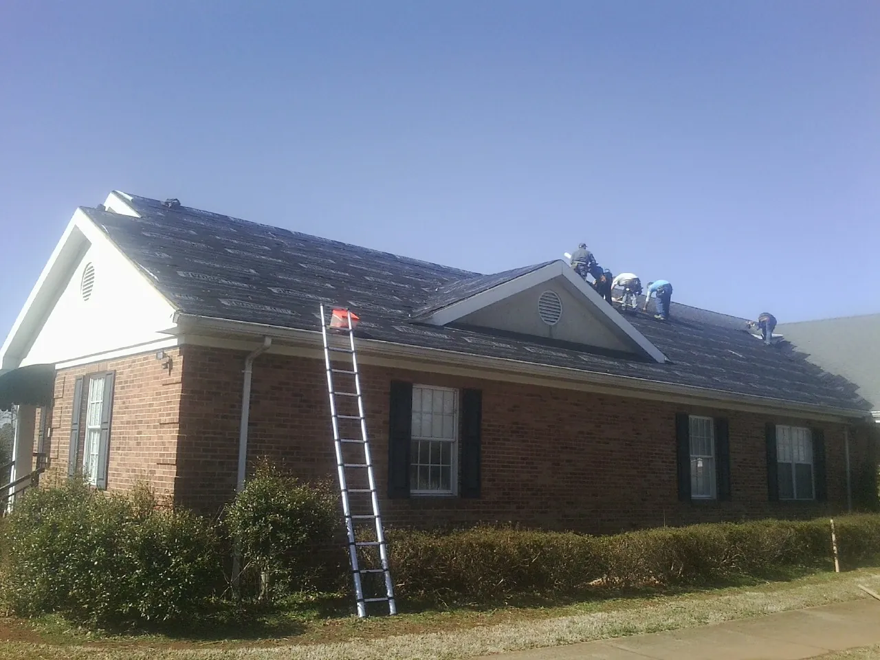 Crew tearing shingles off a brick ranch roof with a ladder set — Emergency Roof Repair work by our crew in Slingerlands