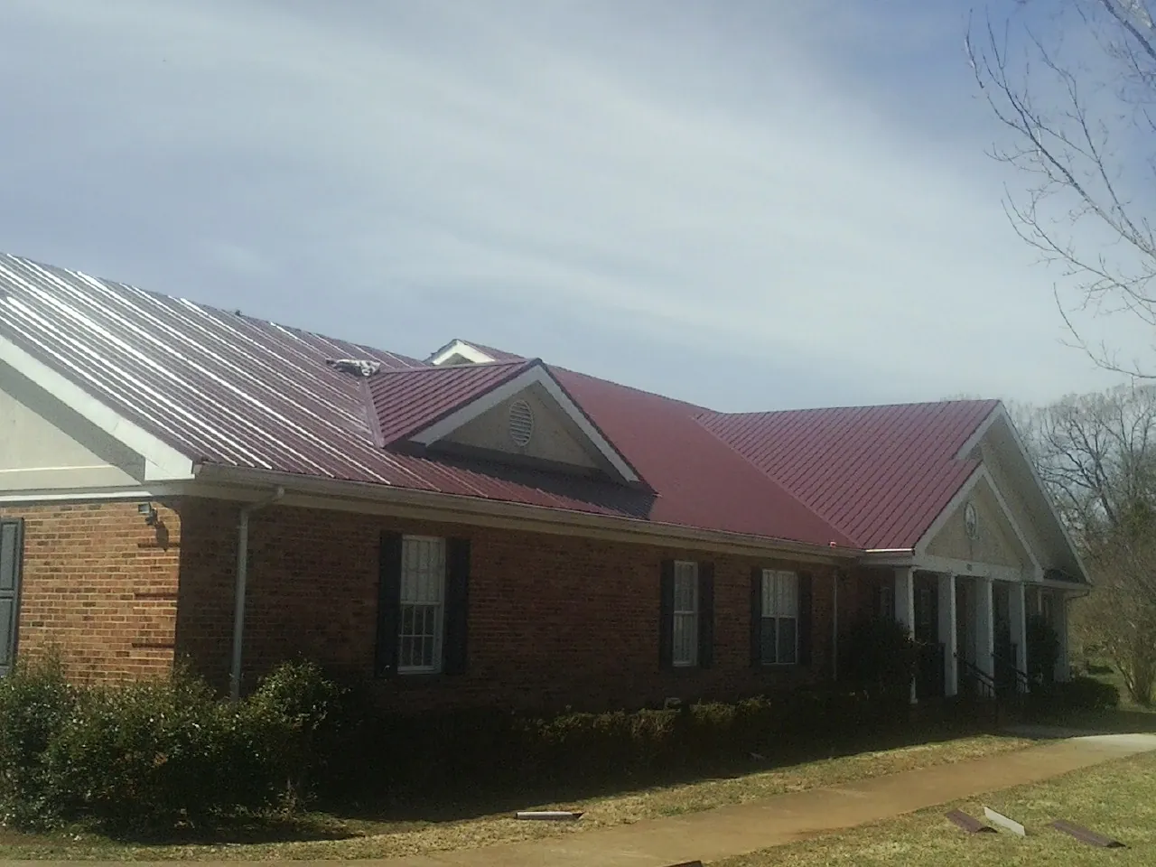 Red metal roof with gabled entries on a long brick building, from a Hail Damage Roof Repair job in Slingerlands