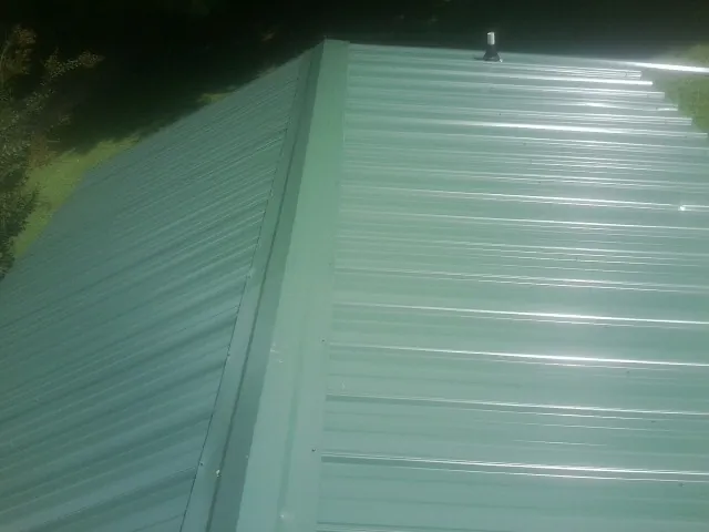 New green metal panels meeting at the ridge of a roof — Flat Roof Repair work by our crew in Slingerlands