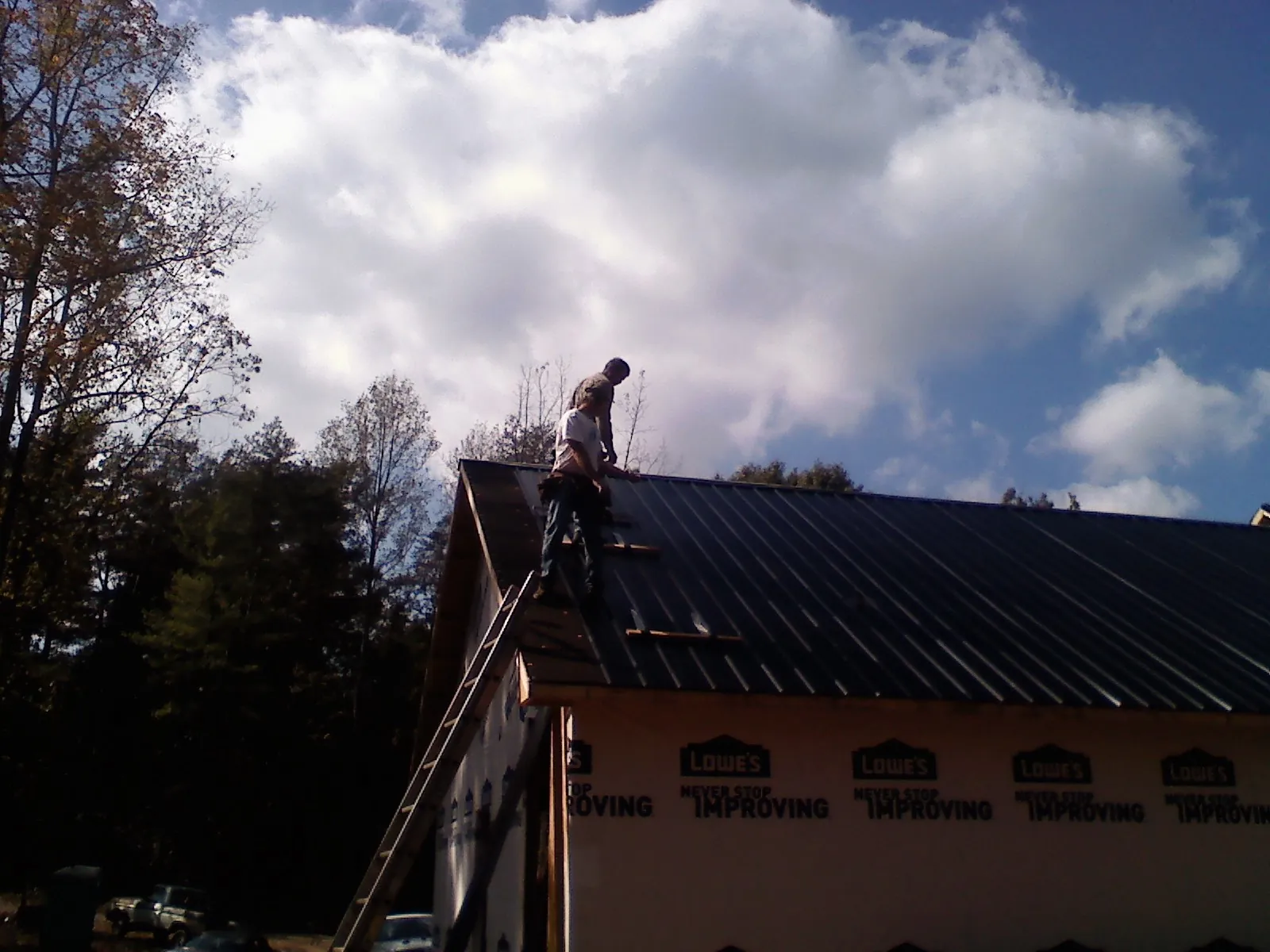 Roofer fastening dark metal panels high against a cloudy sky, from a Roof Inspection job in Slingerlands