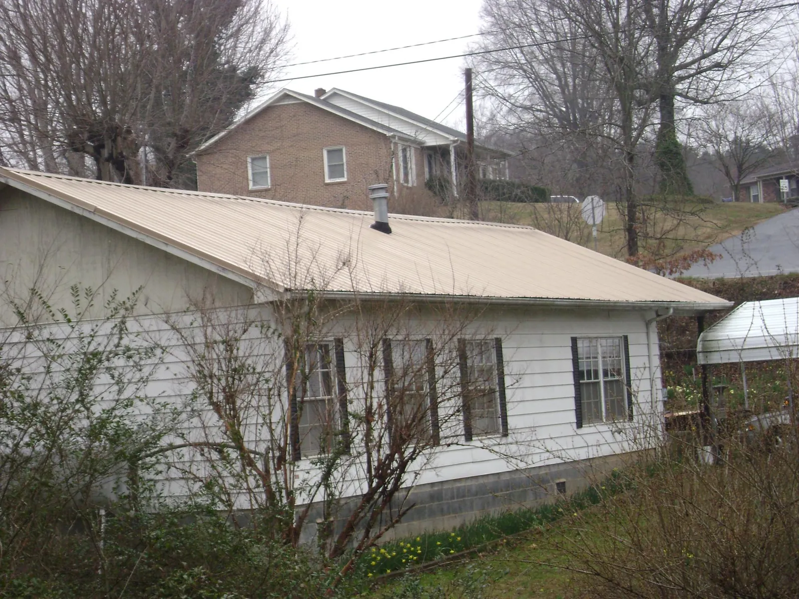 Tan metal roof on a white sided house set into a hillside — Commercial Roofing by Roofing Brothers in Slingerlands